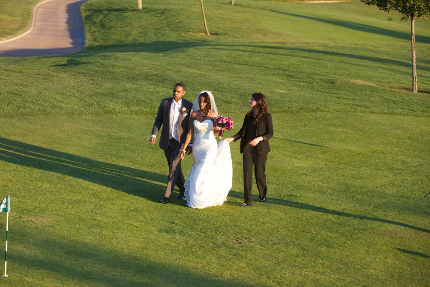 Wedding planner walking with bride and groom and holding bride's dress train